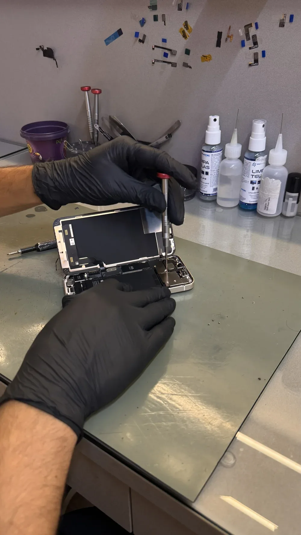 Reparo de celular aberto na bancada da ReeCell, com técnico usando luvas e ferramentas.
