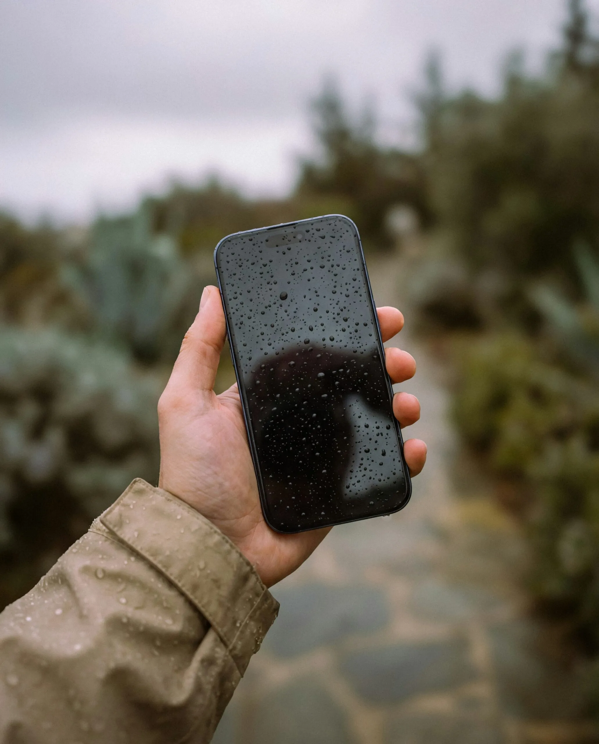 Celular com gotas de água sobre a tela, segurado ao ar livre